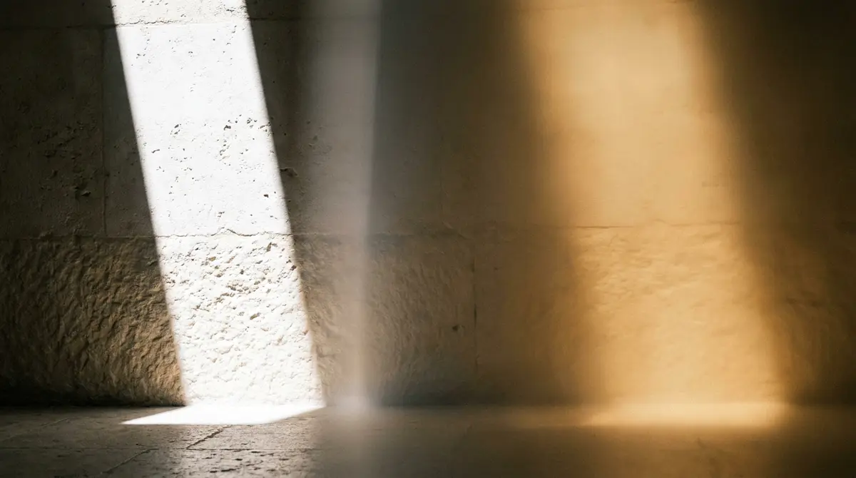 Soft daylight and warm artificial light overlapping on a textured stone wall, symbolising the transformation from harsh glare to a calm, welcoming glow.
